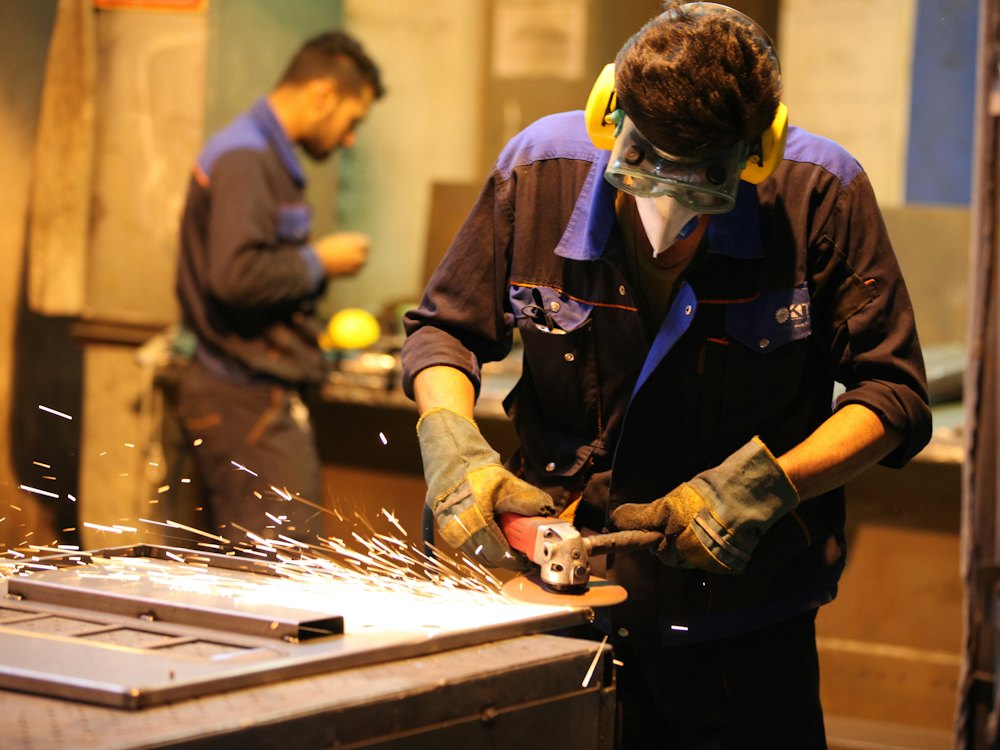 Operaio con cuffie antirumore al lavoro con la smerigliatrice in officina